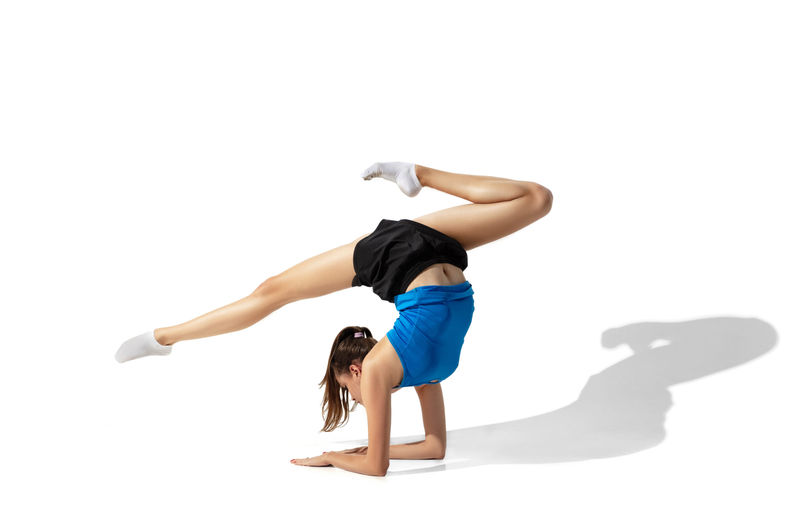 Beautiful young female athlete stretching on white studio background with shadows