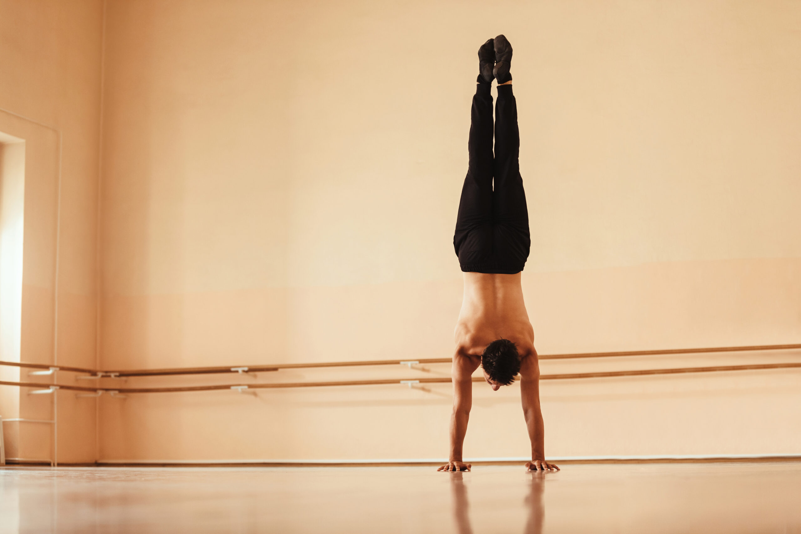 Rear view of male dancer doing handstand at dance studio.
